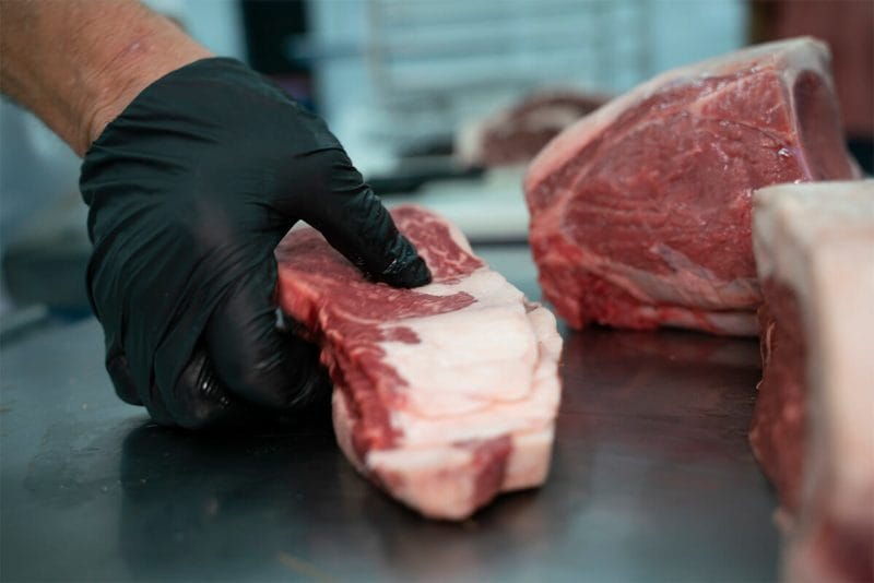 A butcher at 160 Processing is carefully placing a cut of meat on a butchers table.